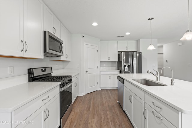 82 Birchfield Ln, Saint Augustine, FL 32092 - kitchen featuring stainless steel appliances, wood finished floors, white cabinetry, pendant lighting, and a kitchen island with sink