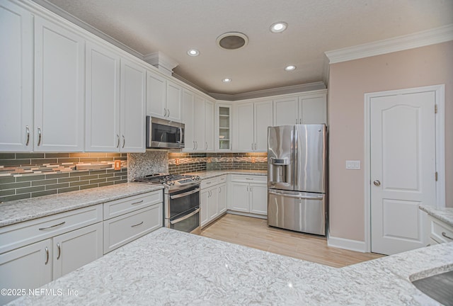 1356 Barrington Cir, Saint Augustine, FL 32092 - kitchen featuring appliances with stainless steel finishes, crown molding, light wood-style floors, glass insert cabinets, and white cabinets