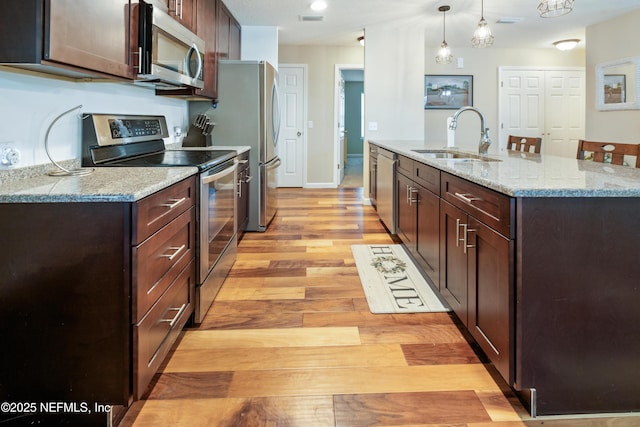 210 N Saint Clair St, Starke, FL 32091 - kitchen featuring stainless steel appliances, light wood-style flooring, hanging light fixtures, dark brown cabinetry, and a kitchen island with sink
