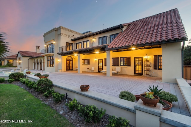 1185 Ponte Vedra Blvd, Ponte Vedra Beach, FL 32082 - back of property at dusk featuring a balcony, stucco siding, a tiled roof, and a patio area