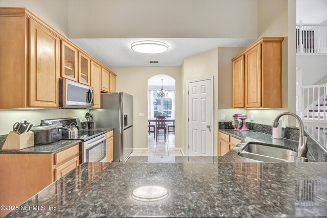 2502 Willow Creek Dr, Fleming Island, FL 32003 - kitchen featuring stainless steel appliances, glass insert cabinets, arched walkways, dark stone countertops, and a chandelier