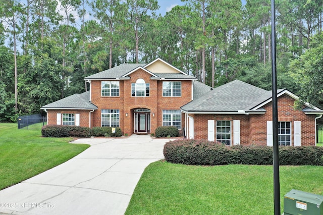 2502 Willow Creek Dr, Fleming Island, FL 32003 - colonial-style house featuring driveway, brick siding, roof with shingles, and a front lawn