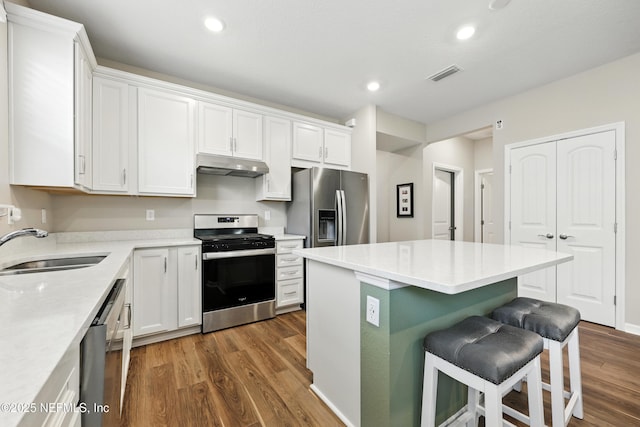 129 Oyster Shell Ter, Ponte Vedra, FL 32081 - kitchen featuring stainless steel appliances, under cabinet range hood, dark wood-type flooring, white cabinetry, and a kitchen breakfast bar