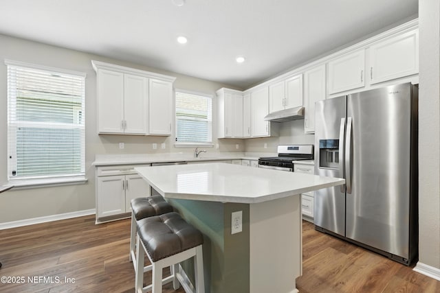 129 Oyster Shell Ter, Ponte Vedra, FL 32081 - kitchen with stainless steel appliances, under cabinet range hood, a breakfast bar, dark wood-style floors, and light countertops