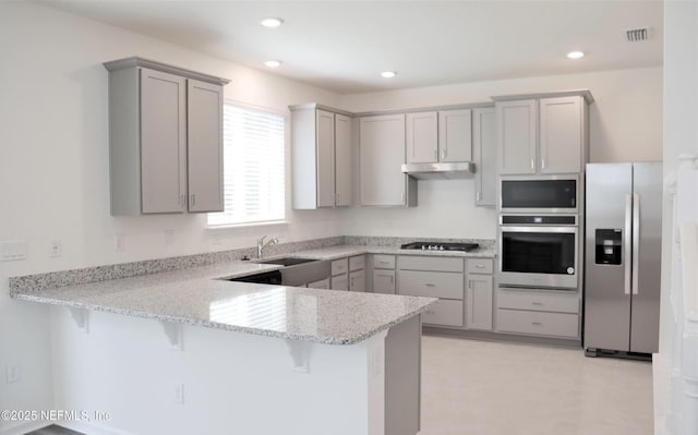 155 Gourd Island Way, Saint Johns, FL 32259 - kitchen with appliances with stainless steel finishes, gray cabinets, a peninsula, a kitchen bar, and under cabinet range hood