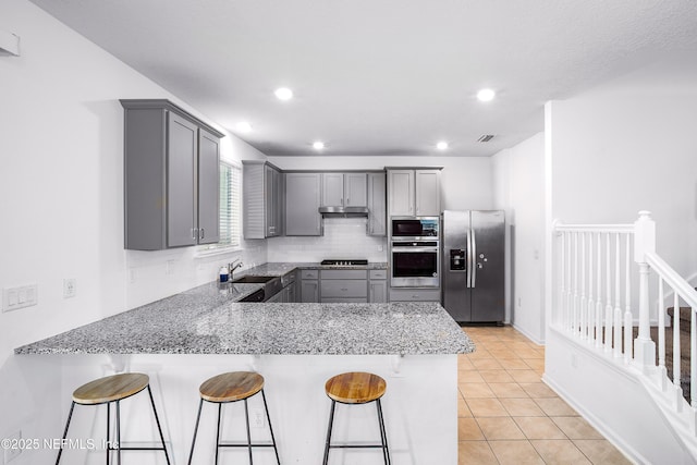 155 Gourd Island Way, Saint Johns, FL 32259 - kitchen with appliances with stainless steel finishes, gray cabinetry, a peninsula, a breakfast bar, and tasteful backsplash