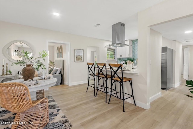 165 Sherry Dr, Atlantic Beach, FL 32233 - kitchen featuring island range hood, fridge, light wood-style floors, a breakfast bar, and white cabinetry