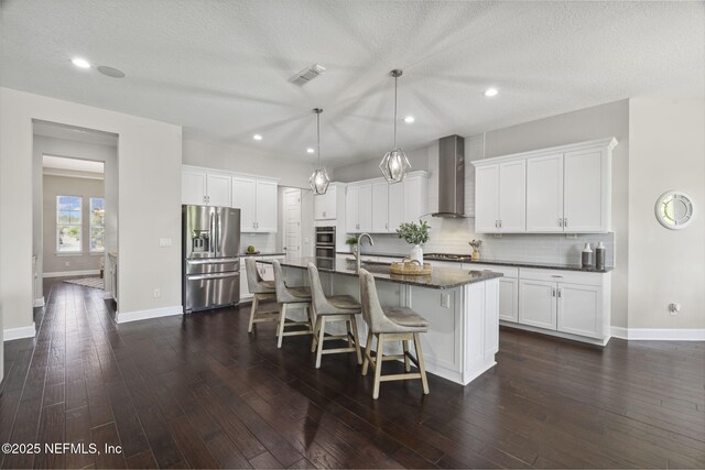 168 Bronson Pkwy, Saint Augustine, FL 32095 - kitchen featuring appliances with stainless steel finishes, wall chimney range hood, a kitchen bar, a center island with sink, and white cabinetry