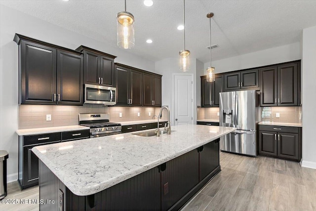 150 Calumet Dr, Saint Johns, FL 32259 - kitchen featuring appliances with stainless steel finishes, an island with sink, light wood-style floors, light stone counters, and a textured ceiling