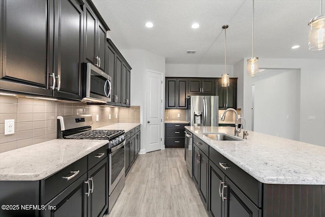 150 Calumet Dr, Saint Johns, FL 32259 - kitchen featuring stainless steel appliances, light wood-style floors, a center island with sink, decorative backsplash, and hanging light fixtures