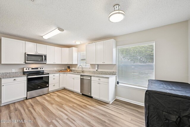96016 Gray Heron Ct, Yulee, FL 32097 - kitchen with appliances with stainless steel finishes, light wood finished floors, white cabinetry, a textured ceiling, and light stone counters