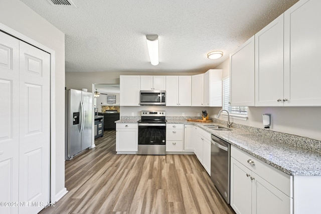 96016 Gray Heron Ct, Yulee, FL 32097 - kitchen featuring appliances with stainless steel finishes, light wood-type flooring, white cabinets, a textured ceiling, and light stone countertops