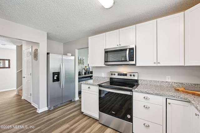 96016 Gray Heron Ct, Yulee, FL 32097 - kitchen featuring appliances with stainless steel finishes, wood finished floors, white cabinetry, a textured ceiling, and light stone counters
