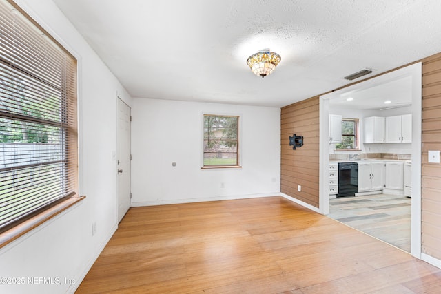 610 Division St, Fernandina Beach, FL 32034 - unfurnished living room featuring light wood finished floors, healthy amount of natural light, a textured ceiling, and wood walls
