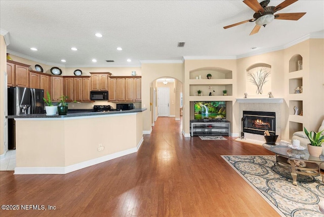 85339 Amagansett Dr, Fernandina Beach, FL 32034 - kitchen featuring black appliances, built in shelves, arched walkways, a fireplace with flush hearth, and a ceiling fan