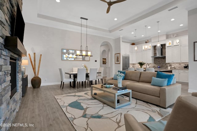 2459 Karatas Ct, Jacksonville, FL 32246 - living area featuring a stone fireplace, a chandelier, arched walkways, a ceiling fan, and light wood-style floors