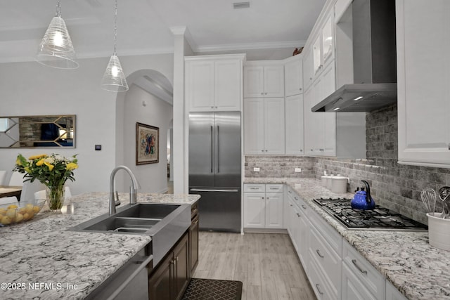 2459 Karatas Ct, Jacksonville, FL 32246 - kitchen with appliances with stainless steel finishes, wall chimney exhaust hood, crown molding, white cabinetry, and light wood-type flooring