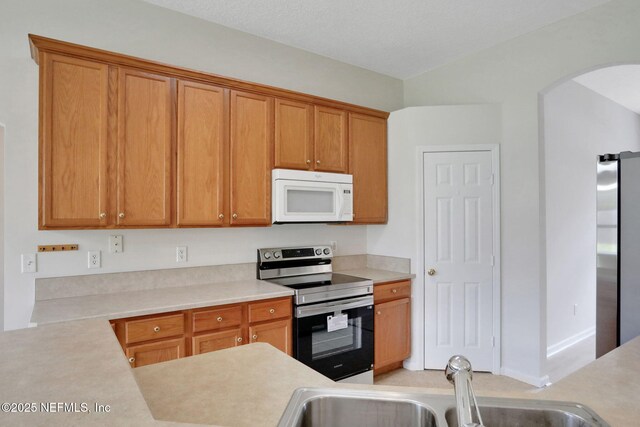 3559 Olympic Dr, Green Cove Springs, FL 32043 - kitchen featuring stainless steel appliances, arched walkways, light countertops, and brown cabinetry