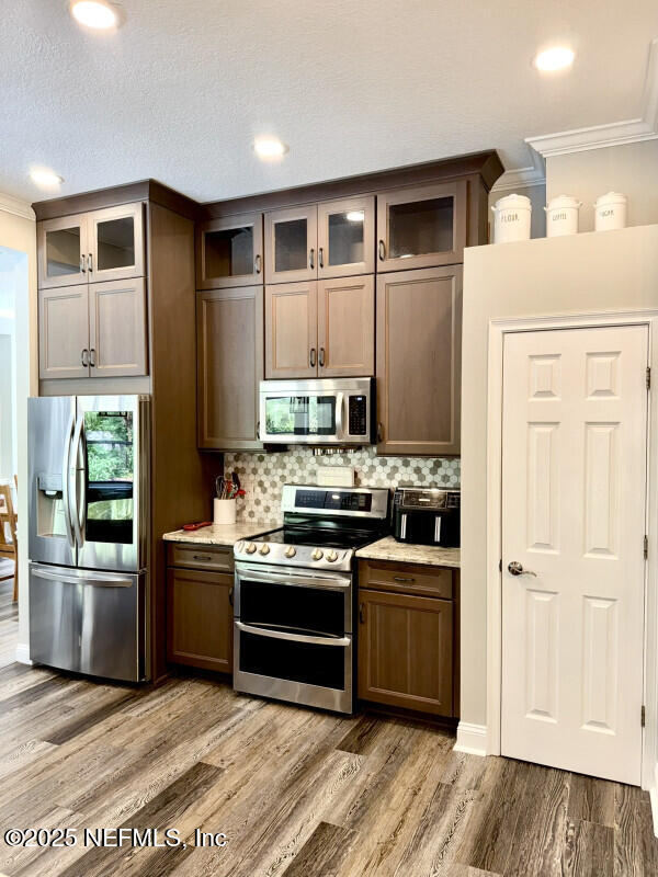 1703 Hunters Ridge Rd, Fleming Island, FL 32003 - kitchen with stainless steel appliances, ornamental molding, decorative backsplash, glass insert cabinets, and recessed lighting