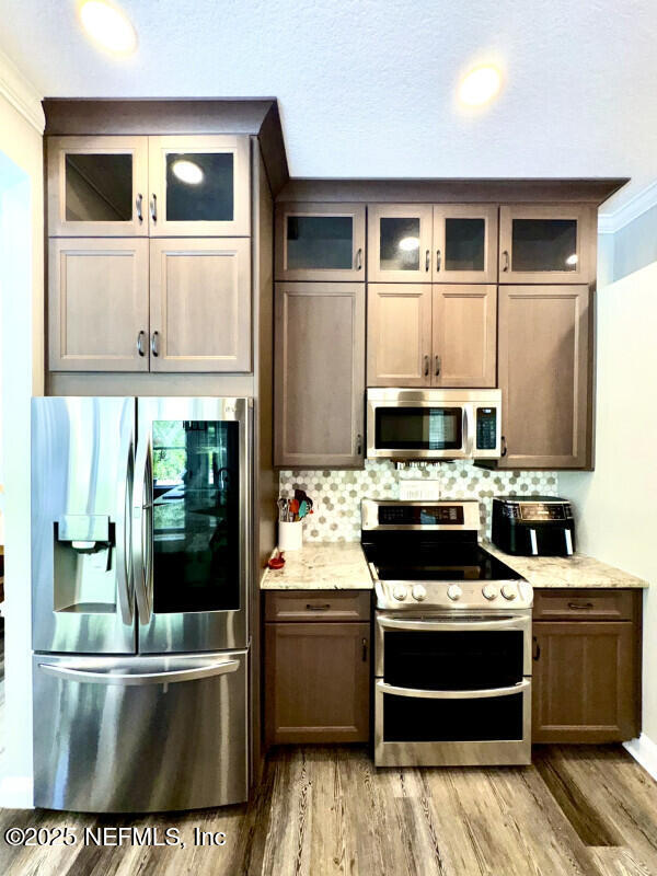 1703 Hunters Ridge Rd, Fleming Island, FL 32003 - kitchen with appliances with stainless steel finishes, light wood-style flooring, tasteful backsplash, crown molding, and glass insert cabinets