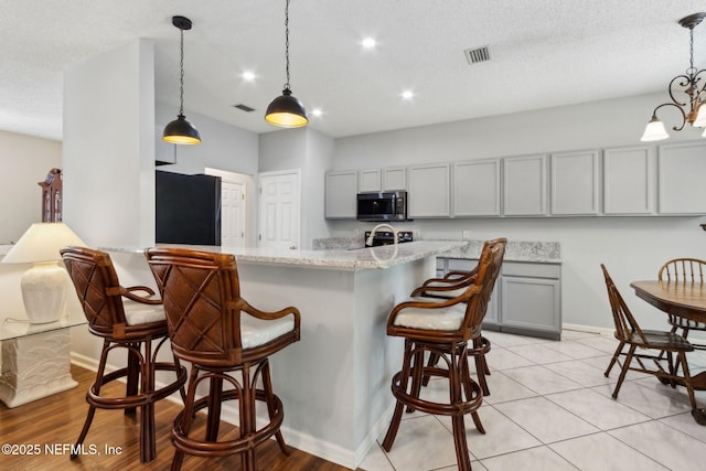 96031 Glen Laurel Ct, Yulee, FL 32097 - kitchen with stainless steel microwave, refrigerator, gray cabinets, a breakfast bar area, and light stone counters