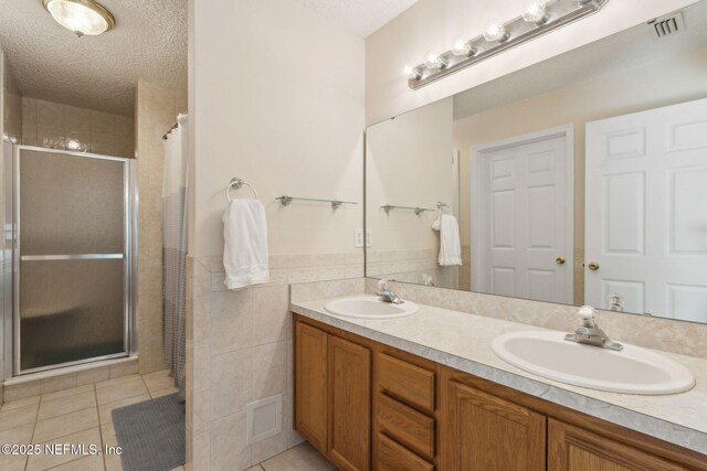 96031 Glen Laurel Ct, Yulee, FL 32097 - bathroom featuring tile patterned floors, a stall shower, double vanity, a textured ceiling, and tile walls