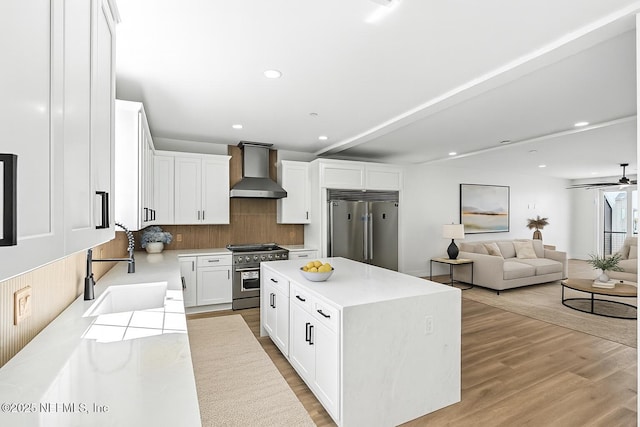 82 Cortez Ave, Saint Augustine, FL 32080 - kitchen with high end appliances, wall chimney range hood, tasteful backsplash, light wood-style flooring, and white cabinetry