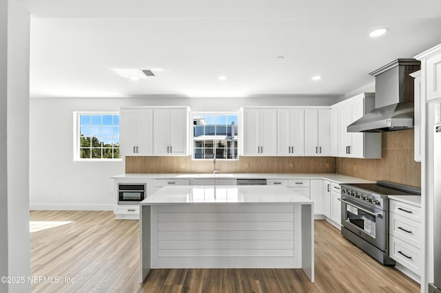 82 Cortez Ave, Saint Augustine, FL 32080 - kitchen featuring appliances with stainless steel finishes, wall chimney exhaust hood, backsplash, light countertops, and light wood-style flooring