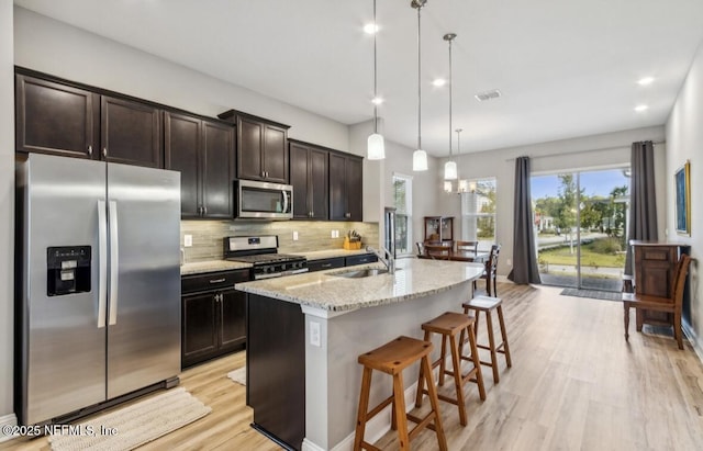 240 Julep St, Yulee, FL 32097 - kitchen featuring appliances with stainless steel finishes, light wood finished floors, tasteful backsplash, light stone counters, and a center island with sink