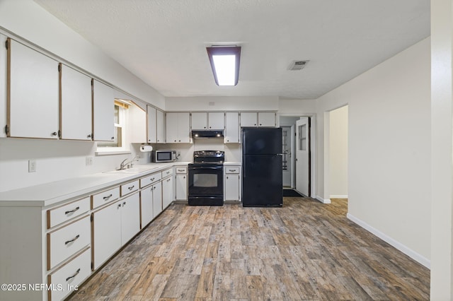 136 Hollywood Forest Dr, Fleming Island, FL 32003 - kitchen with black appliances, light countertops, light wood-style floors, under cabinet range hood, and white cabinetry