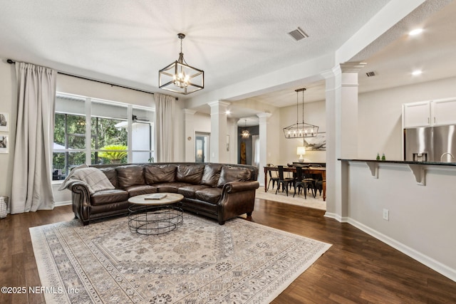 95006 Buckeye Ct, Fernandina Beach, FL 32034 - living room featuring ornate columns, a chandelier, dark wood-style flooring, and a textured ceiling