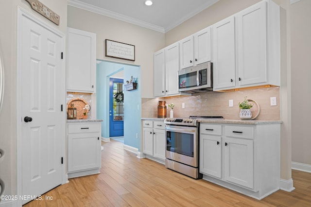 96740 Quartz Ln, Yulee, FL 32097 - kitchen with appliances with stainless steel finishes, crown molding, light wood finished floors, white cabinets, and tasteful backsplash