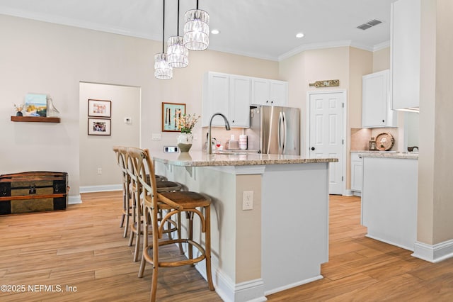 96740 Quartz Ln, Yulee, FL 32097 - kitchen featuring freestanding refrigerator, a breakfast bar area, light stone countertops, white cabinets, and crown molding