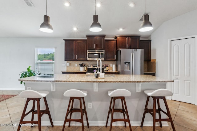 95297 Windflower Trl, Fernandina Beach, FL 32034 - kitchen with stainless steel appliances, decorative backsplash, light tile patterned floors, dark brown cabinetry, and a breakfast bar