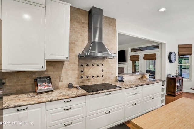 1805 Commodore Point Dr, Fleming Island, FL 32003 - kitchen with wall chimney range hood, black electric cooktop, white cabinetry, light stone counters, and decorative backsplash