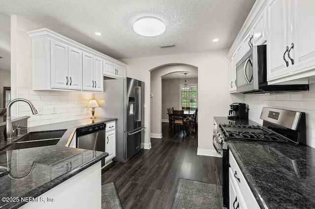 26122 Sheared Stokes Rd, Hilliard, FL 32046 - kitchen featuring appliances with stainless steel finishes, arched walkways, white cabinets, dark wood-type flooring, and dark stone countertops