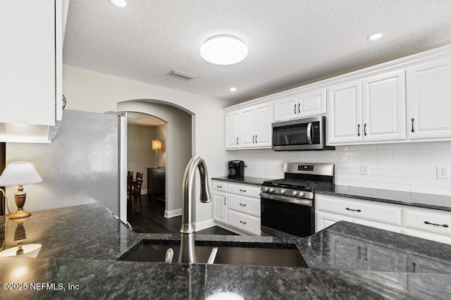 26122 Sheared Stokes Rd, Hilliard, FL 32046 - kitchen featuring appliances with stainless steel finishes, arched walkways, white cabinets, backsplash, and dark stone countertops