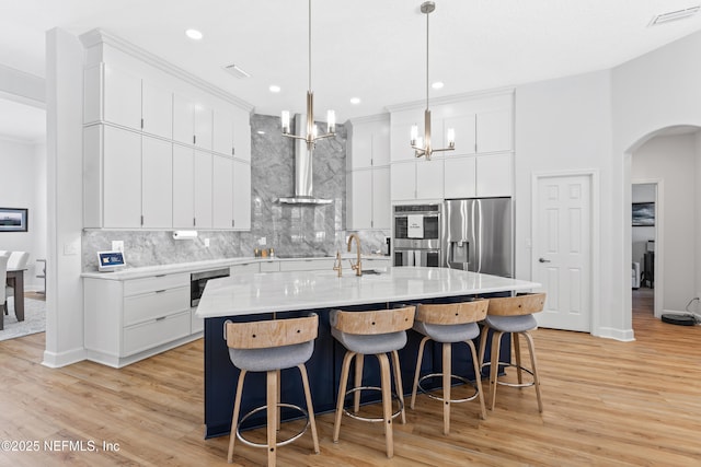 1317 Garrison Dr, Saint Augustine, FL 32092 - kitchen featuring appliances with stainless steel finishes, arched walkways, tasteful backsplash, light wood-style floors, and a kitchen island with sink
