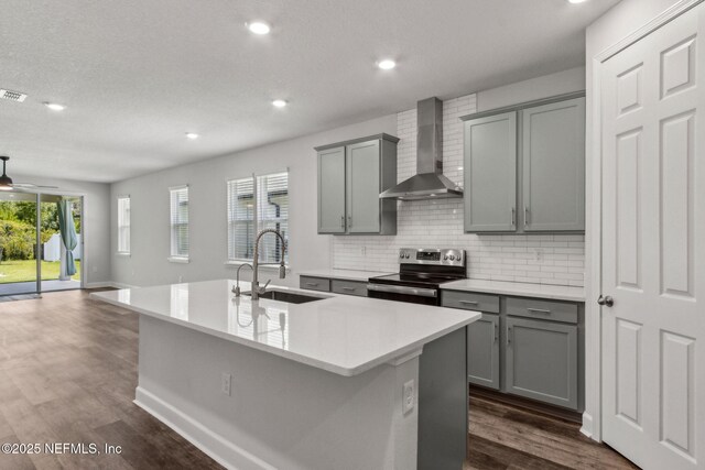 94954 Colnago Ct, Fernandina Beach, FL 32034 - kitchen featuring stainless steel range with electric stovetop, gray cabinetry, wall chimney exhaust hood, a center island with sink, and tasteful backsplash