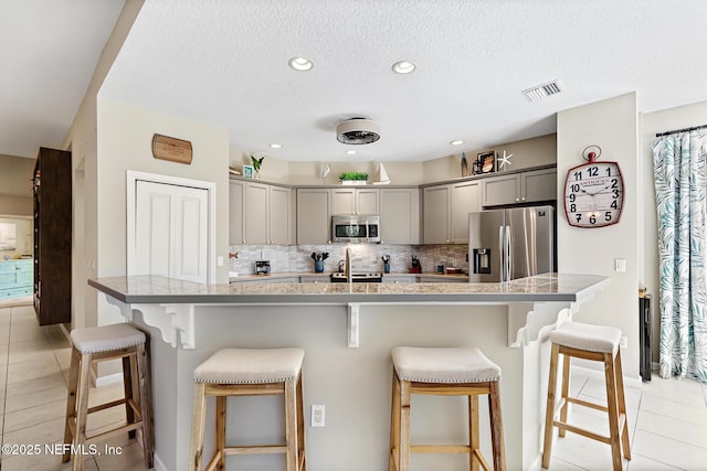 308 High Tide Dr Unit 201, Saint Augustine, FL 32080 - kitchen featuring appliances with stainless steel finishes, gray cabinetry, light tile patterned floors, a kitchen breakfast bar, and tasteful backsplash