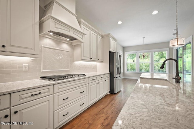 305 Seahill Dr, Saint Augustine, FL 32092 - kitchen with custom exhaust hood, stainless steel appliances, hanging light fixtures, wood finished floors, and light stone counters