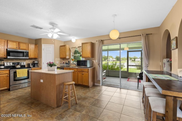 76146 Long Leaf Loop, Yulee, FL 32097 - kitchen featuring stainless steel appliances, tasteful backsplash, ceiling fan, a center island, and arched walkways