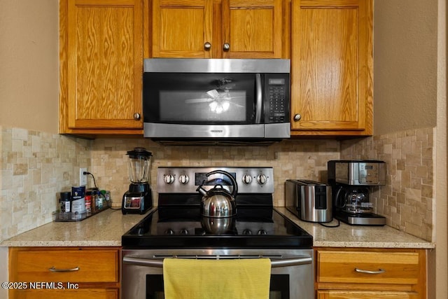 76146 Long Leaf Loop, Yulee, FL 32097 - kitchen with appliances with stainless steel finishes, brown cabinetry, decorative backsplash, and light stone counters