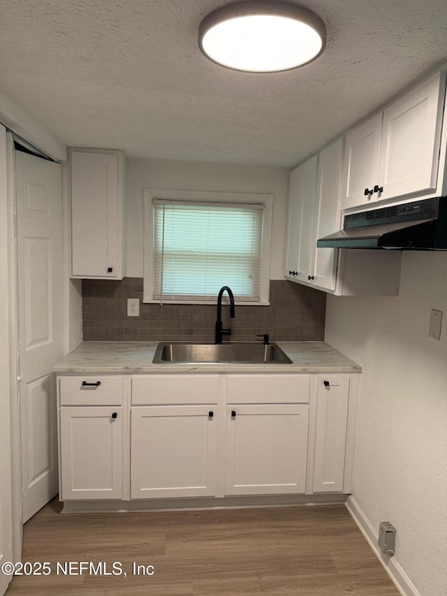 7536 Wakefield Ave, Jacksonville, FL 32208 - kitchen with under cabinet range hood, decorative backsplash, light wood finished floors, white cabinetry, and a textured ceiling