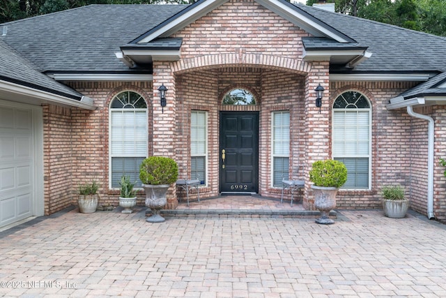 6992 Tonga Dr, Jacksonville, FL 32216 - view of exterior entry featuring a shingled roof, brick siding, an attached garage, and decorative driveway