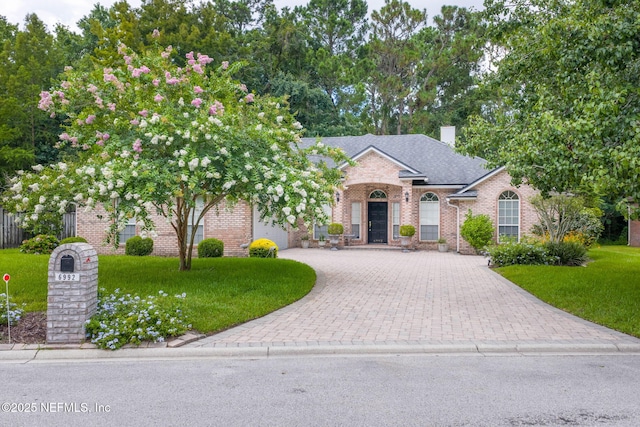6992 Tonga Dr, Jacksonville, FL 32216 - view of front of home with decorative driveway, a front yard, brick siding, and a chimney