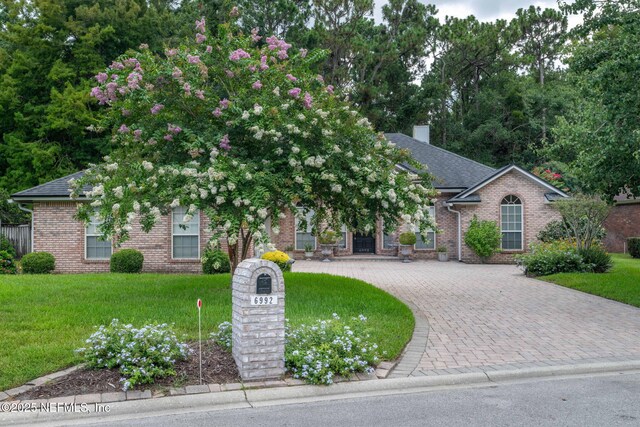 6992 Tonga Dr, Jacksonville, FL 32216 - obstructed view of property featuring brick siding, curved driveway, a front yard, and a chimney