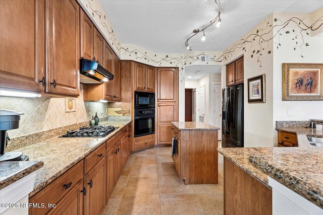 201 S Ocean Grande Dr Unit 104, Ponte Vedra Beach, FL 32082 - kitchen featuring black appliances, under cabinet range hood, light stone countertops, brown cabinets, and a textured ceiling