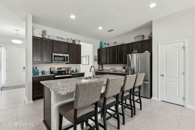 86180 Tranquil Ct, Yulee, FL 32097 - kitchen featuring appliances with stainless steel finishes, a breakfast bar, light tile patterned floors, dark brown cabinets, and a textured ceiling