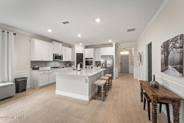 75013 Pondside Ln, Yulee, FL 32097 - kitchen featuring stainless steel appliances, ornamental molding, a kitchen island with sink, light countertops, and white cabinets